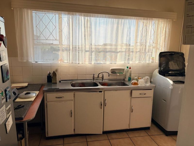 A functional laundry area featuring a stainless steel double sink, tiled splashback, and built-in cabinetry with tiled flooring.