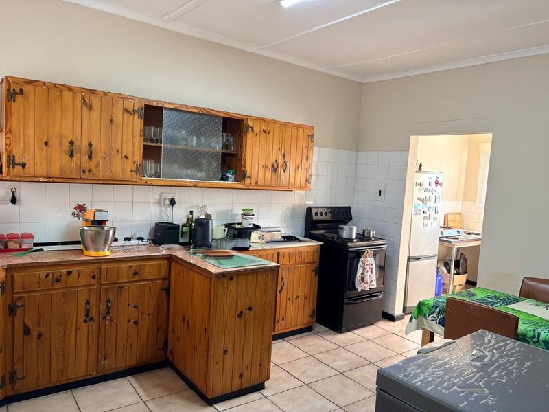 A functional kitchen featuring traditional pine cabinetry, tiled backsplash, and ceramic flooring, with an adjoining scullery area.