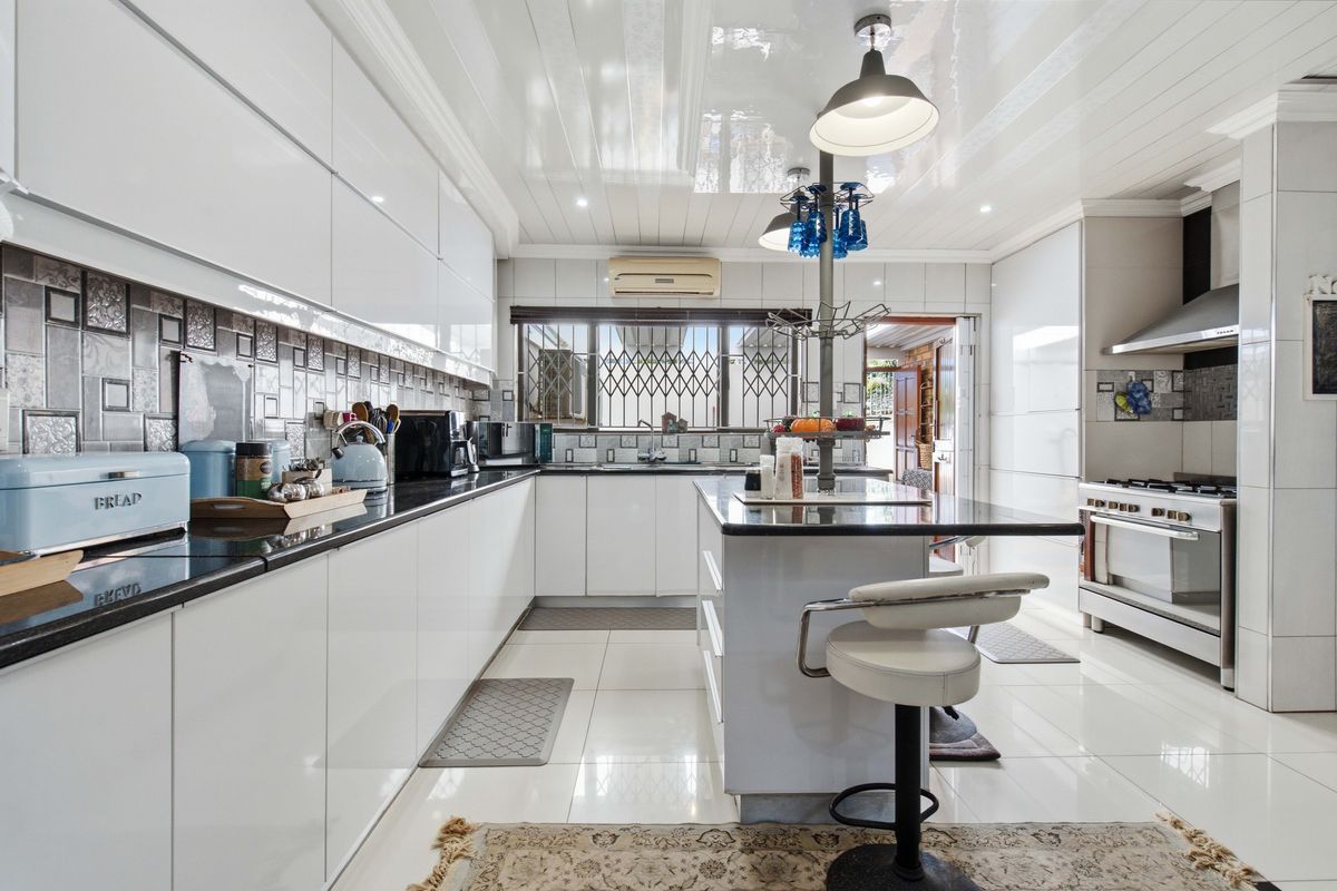 Modern kitchen featuring high-gloss white cabinetry, black granite countertops, a central island, and stainless steel appliances, complemented by polished floor tiles and a glossy ceiling.