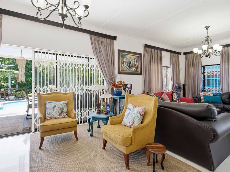 Spacious living room featuring tiled flooring, elegant chandeliers, and large sliding glass doors that provide direct access to the outdoor pool area.