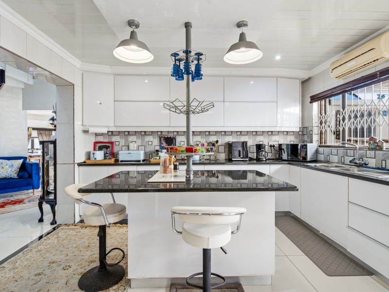 Modern kitchen featuring glossy white cabinetry, a central island with granite countertops, tiled backsplash, and integrated lighting, offering a functional and bright workspace.