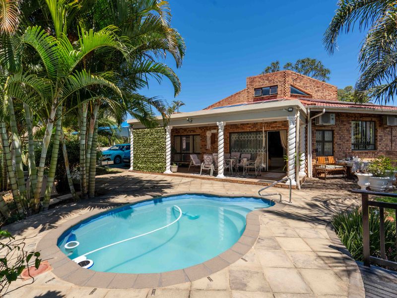 A well-maintained rear garden area featuring a swimming pool, paved patio, and a brick-built house with a covered outdoor entertainment space.