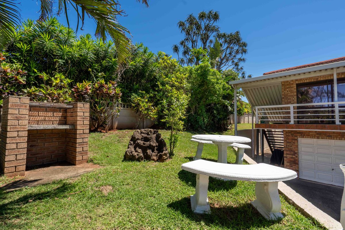 A private rear garden featuring a built-in brick braai, established landscaping, and a covered patio area with concrete seating.
