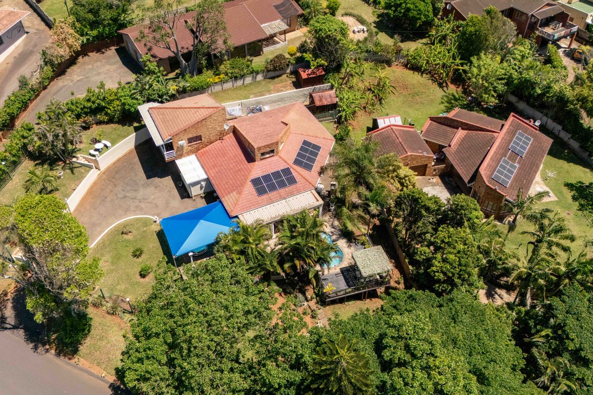 Aerial view of a residential property featuring a tiled roof with solar panels, a swimming pool, a wooden deck, and a paved driveway.