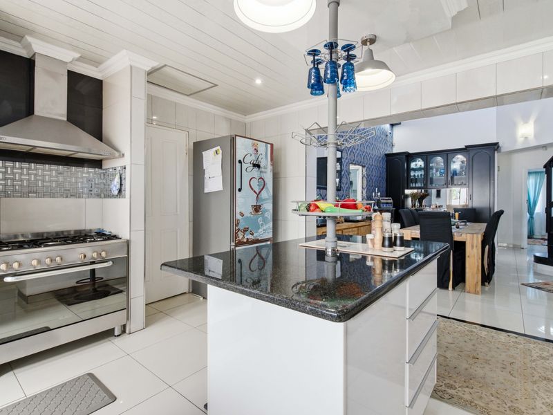 Modern open-plan kitchen featuring a central island with granite countertops, stainless steel gas stove, and sleek cabinetry, flowing into the adjacent dining area.