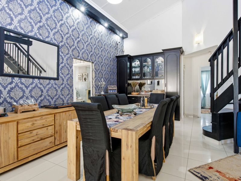 Spacious dining area featuring high ceilings, decorative wallpaper, built-in cabinetry, and a staircase leading to the upper level with polished tiled flooring throughout.