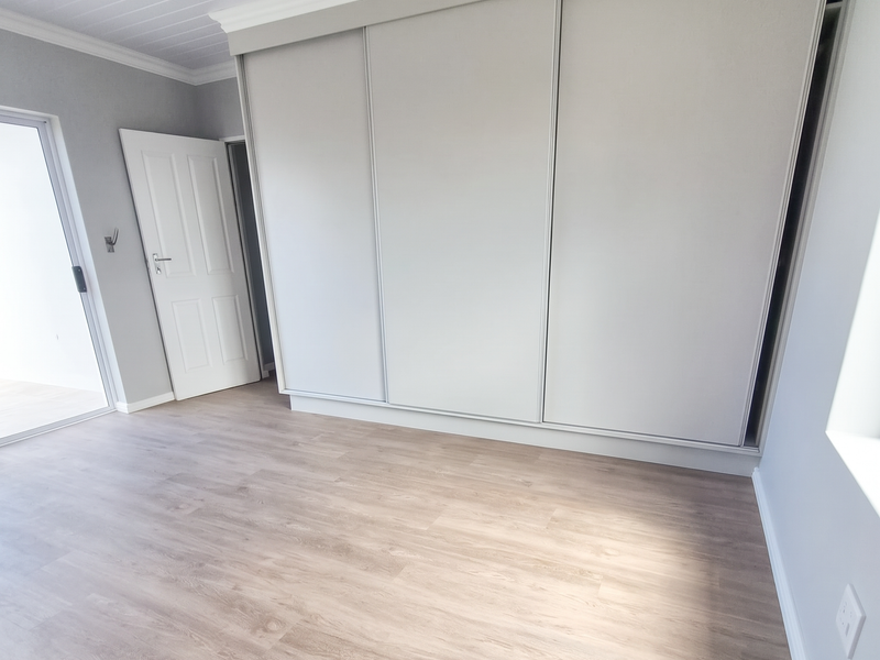 A bright, empty bedroom featuring modern laminate flooring, a large built-in sliding wardrobe, and a clean tongue and groove ceiling finish.