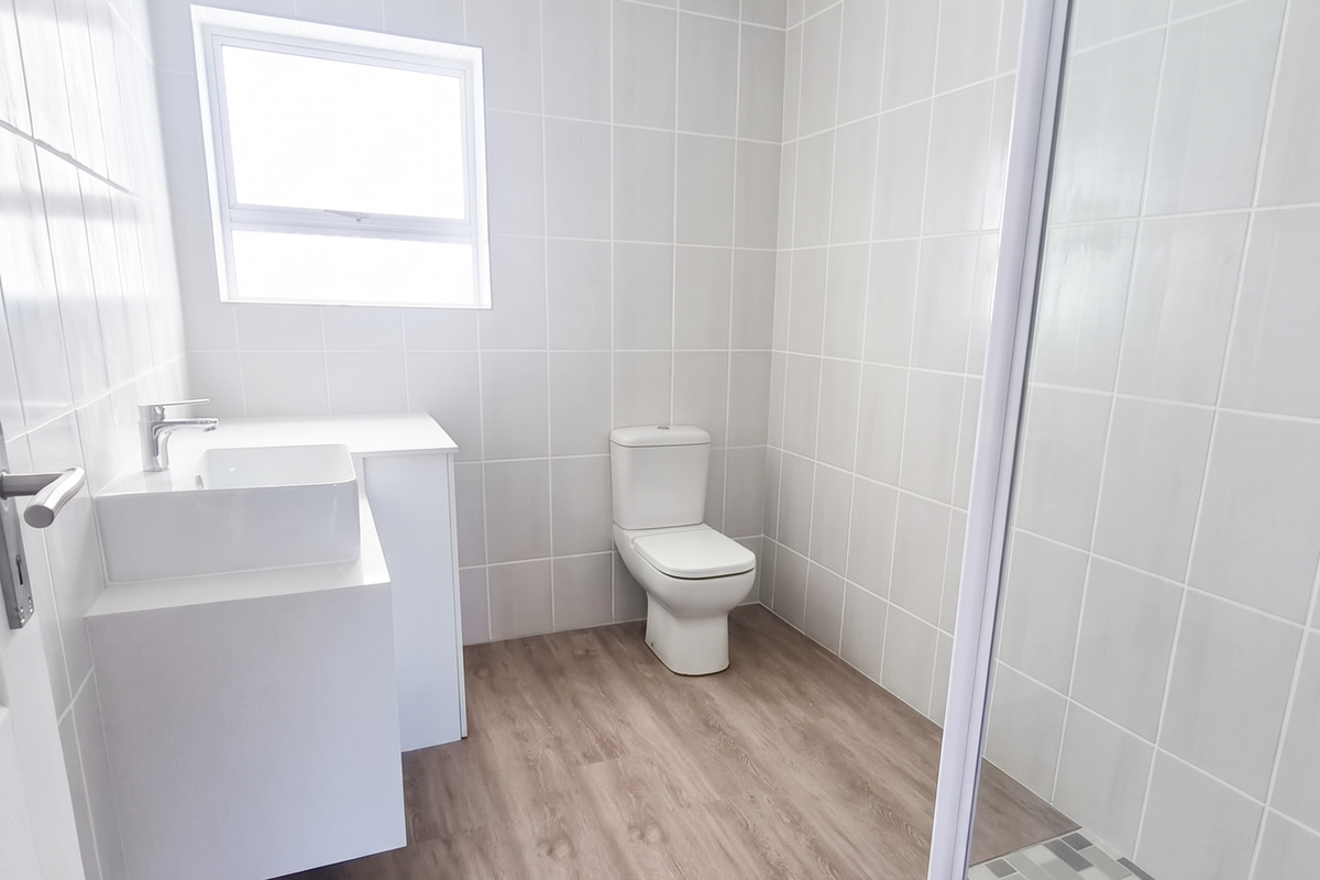 A modern, clean bathroom featuring a wall-mounted vanity, a white toilet, and a glass-enclosed shower with neutral wall tiling and wood-look flooring.