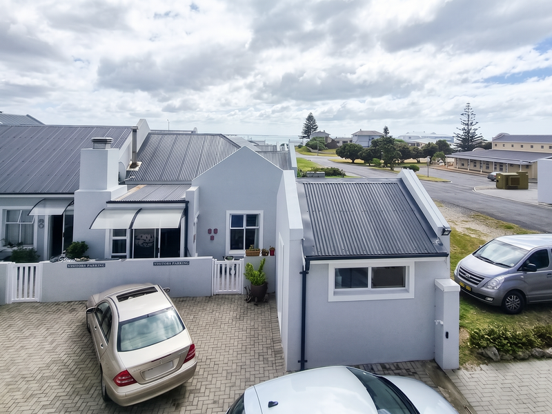 Elevated view of the apartment complex front exterior, featuring a paved driveway, corrugated metal roofing, and secure boundary walling.