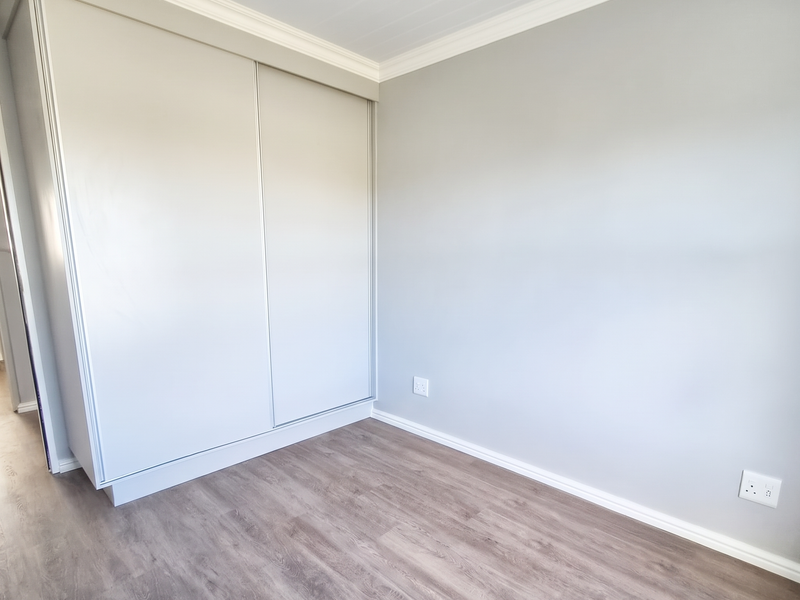 A clean, modern bedroom featuring neutral grey walls, wood-look laminate flooring, and a spacious built-in sliding door wardrobe.