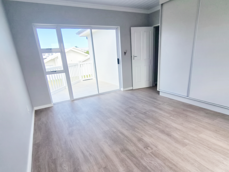 A bright, empty bedroom featuring modern laminate flooring, built-in sliding wardrobes, and direct access to a private balcony through sliding glass doors.