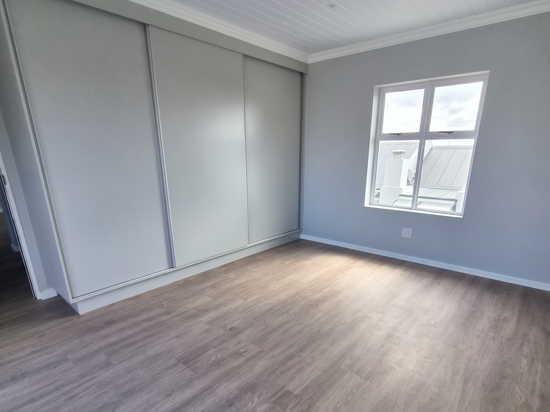 A bright, empty bedroom featuring modern laminate flooring, a large built-in sliding wardrobe, and a clean tongue and groove ceiling with recessed lighting.