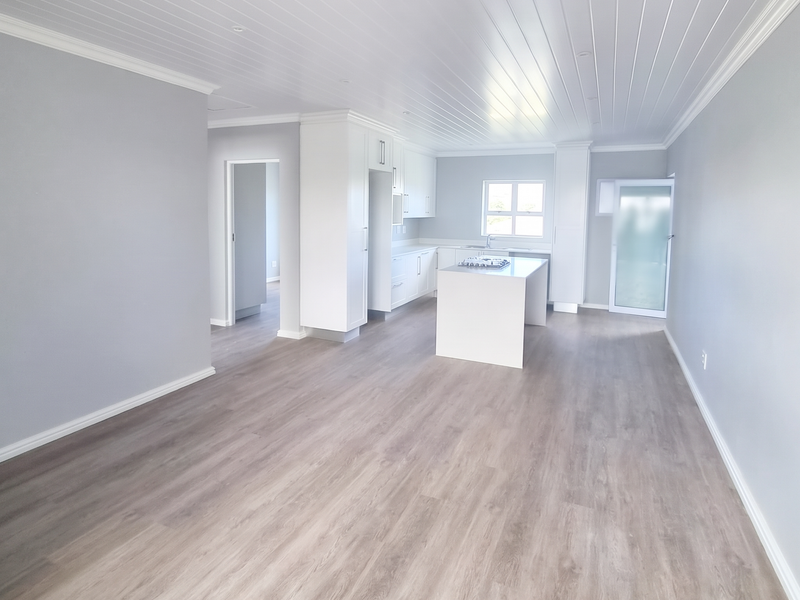 Spacious open-plan living and kitchen area featuring modern laminate flooring, a central kitchen island with a hob, and a clean, neutral aesthetic.