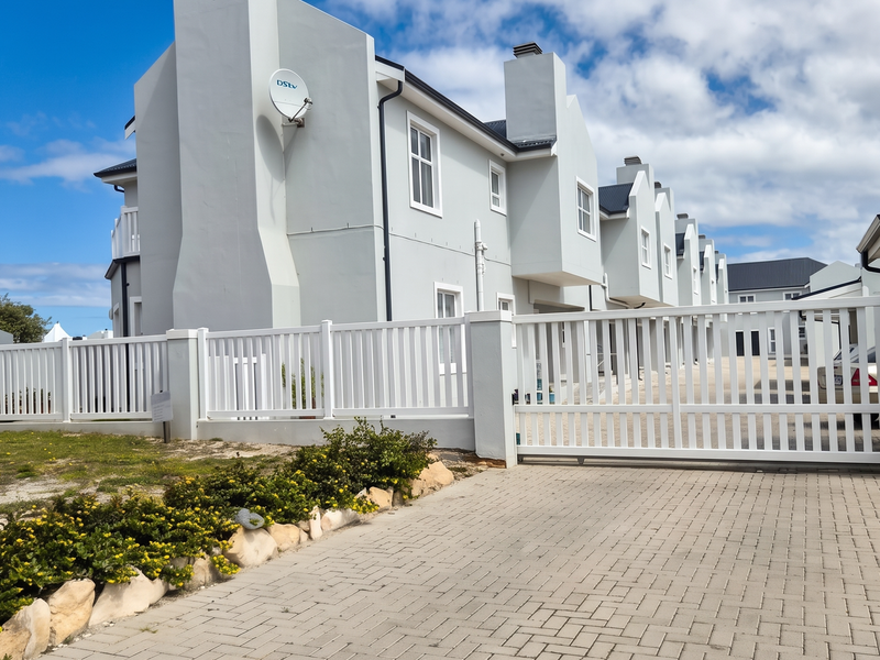 Front view of a modern apartment complex featuring a paved driveway, secure white fencing, and gated access.