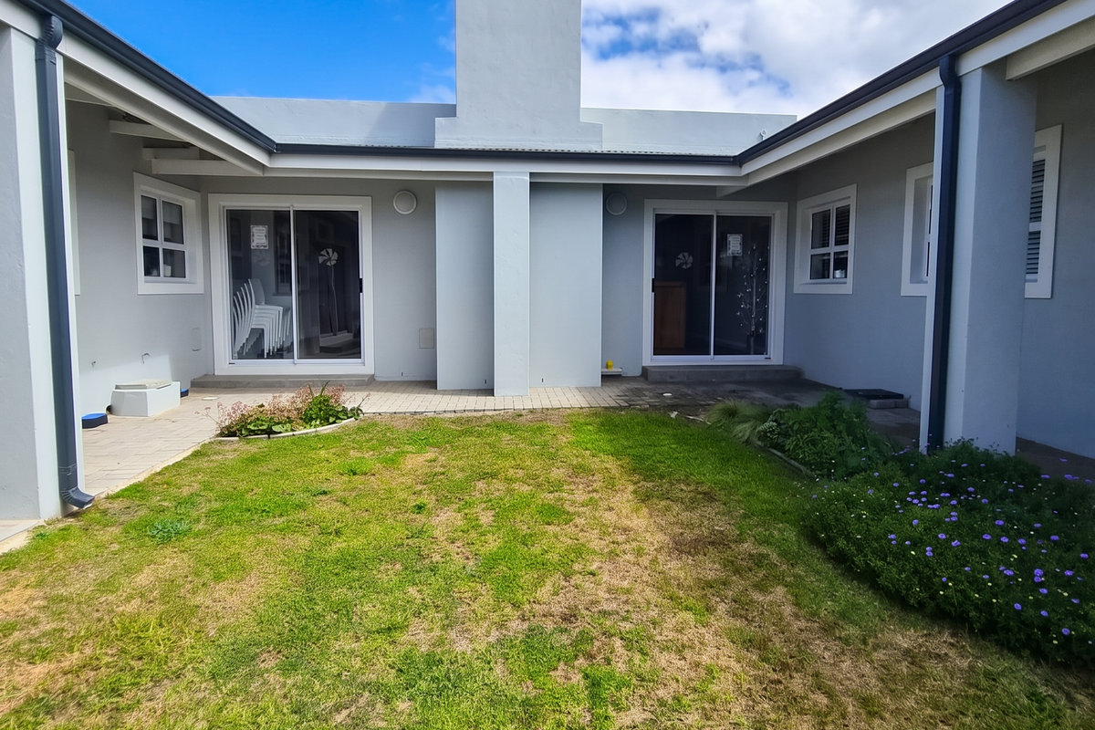 Rear view of the property featuring a central chimney, dual sliding glass doors, and a paved patio area overlooking a lawn.