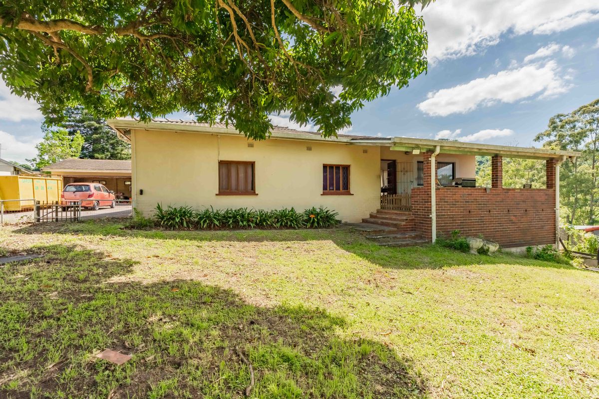 Rear view of the house featuring a covered brick patio, lawn area, and a detached garage with driveway access.