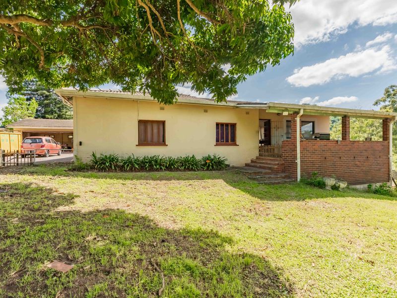 Rear view of the house featuring a covered brick patio, lawn area, and a detached garage with driveway access.