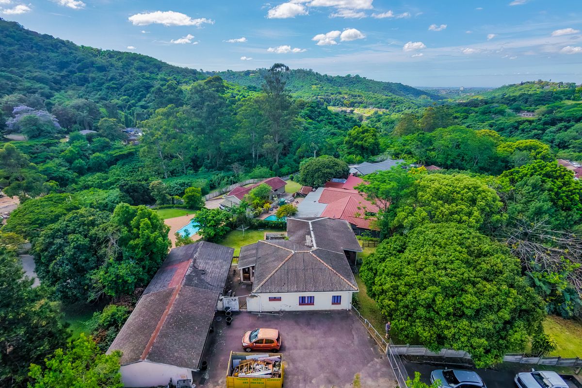Aerial view of a residential property featuring a tiled roof house, asphalt driveway, and swimming pool, set within a lush, green landscape.