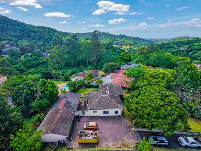Aerial view of a residential property featuring a tiled roof house, asphalt driveway, and swimming pool, set within a lush, green landscape.