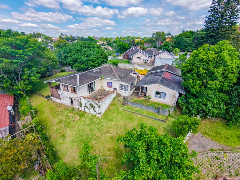 Aerial view of a residential property featuring a main house and secondary structure set within a large, established garden with mature trees.