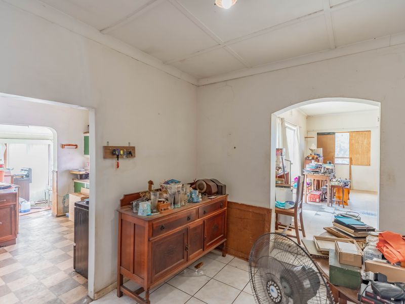 A living area featuring tiled flooring and arched doorways leading to adjacent rooms, showing signs of wear and requiring cosmetic updates.