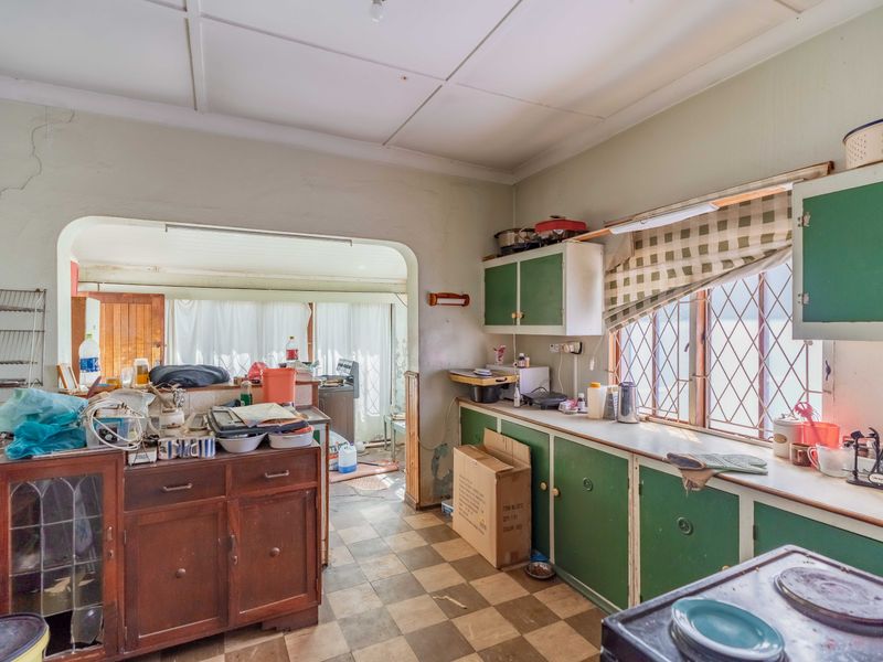 A dated kitchen featuring original cabinetry, tiled flooring, and diamond-patterned windows, requiring significant renovation and cosmetic updates to modernize the space.