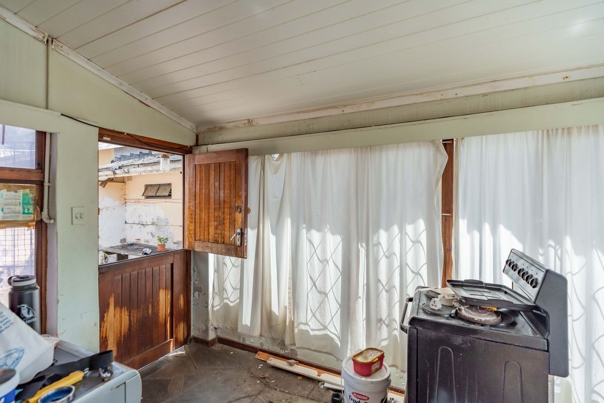A rustic kitchen area featuring stone flooring, a timber ceiling, and a traditional stable door, currently requiring significant cosmetic renovation and repair.