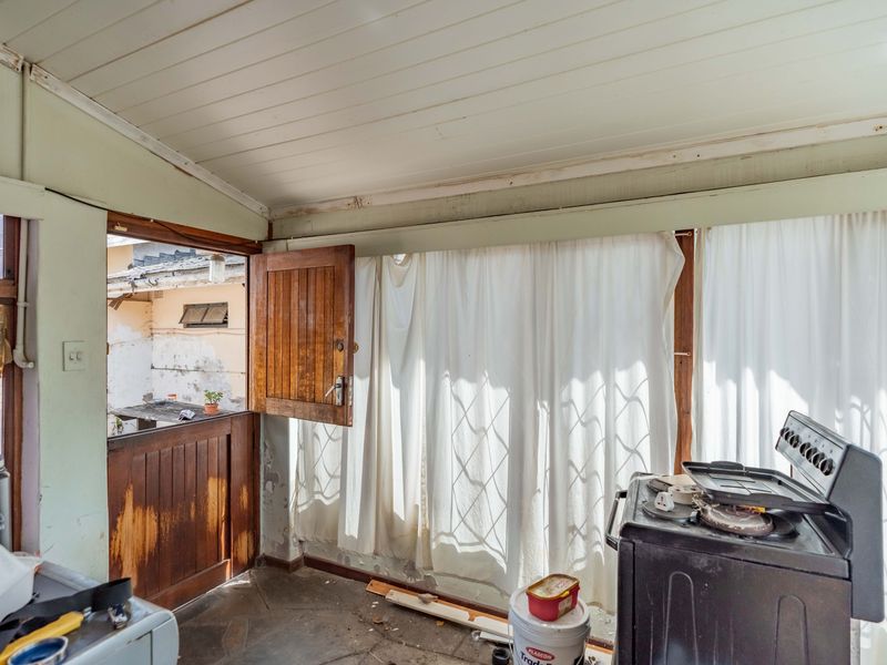 A rustic kitchen area featuring stone flooring, a timber ceiling, and a traditional stable door, currently requiring significant cosmetic renovation and repair.