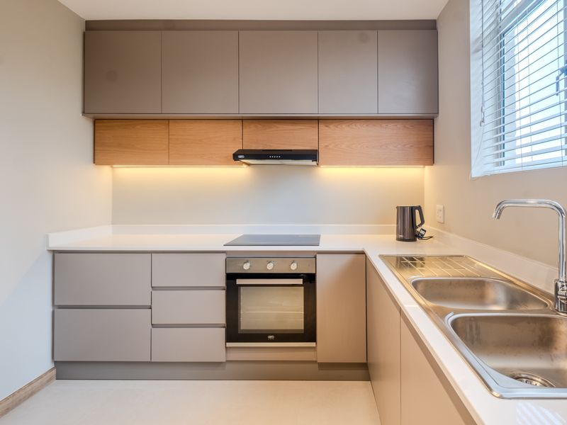 Modern kitchen featuring sleek two-tone cabinetry, stone countertops, integrated stainless steel sink, and built-in appliances including an electric hob and oven.
