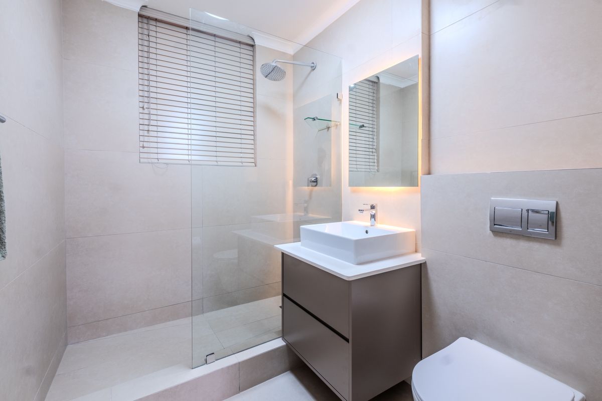 Modern bathroom featuring a walk-in shower with glass screen, wall-mounted vanity with vessel sink, backlit mirror, and a concealed cistern toilet.