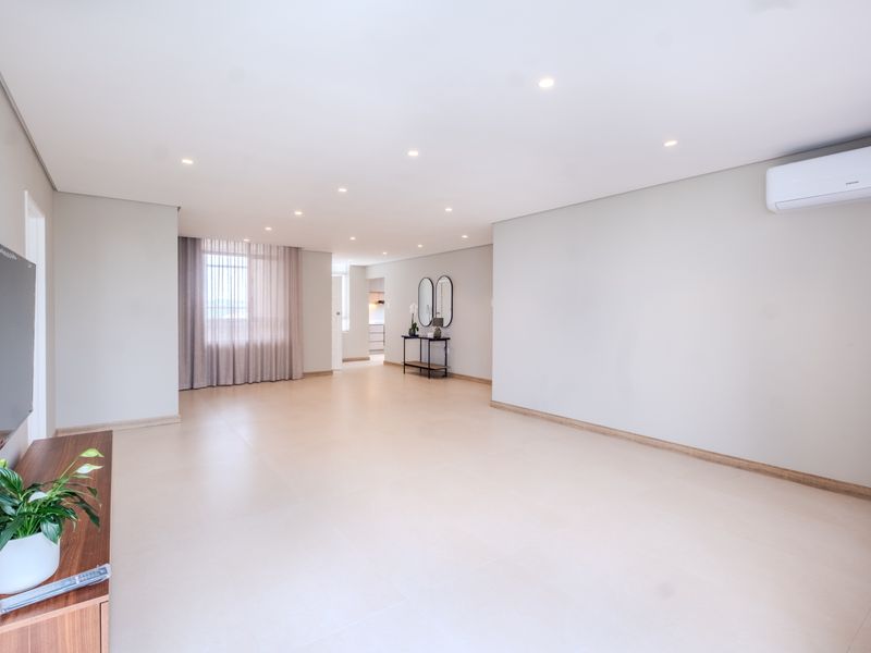 Spacious and bright open-plan living area featuring neutral tiled flooring, recessed downlighting, and a wall-mounted air conditioning unit.