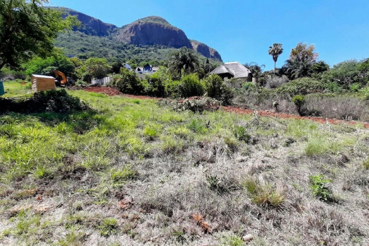 A view of a vacant residential plot featuring natural vegetation and scenic mountain views in the background.