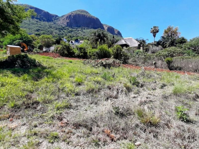 A view of a vacant residential plot featuring natural vegetation and scenic mountain views in the background.