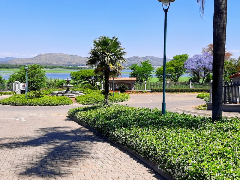 A well-maintained residential estate entrance featuring paved driveways, landscaped gardens, a central stone fountain, and scenic views of the surrounding landscape.