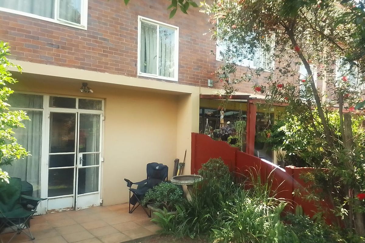 Rear view of the apartment featuring a brick facade, tiled patio area, and direct access through sliding glass doors to the garden space.