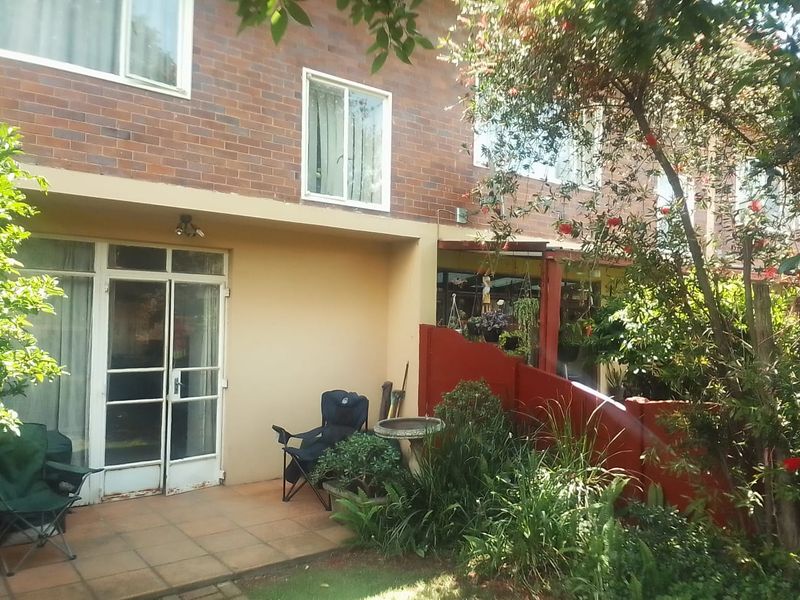 Rear view of the apartment featuring a brick facade, tiled patio area, and direct access through sliding glass doors to the garden space.
