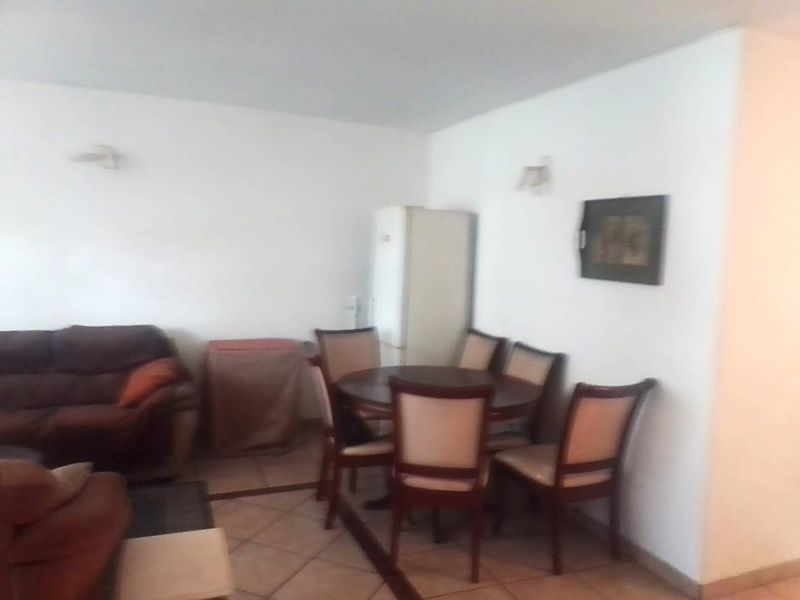 An open-plan living and dining area featuring tiled flooring and wall-mounted lighting, offering a functional space for relaxation and meals.