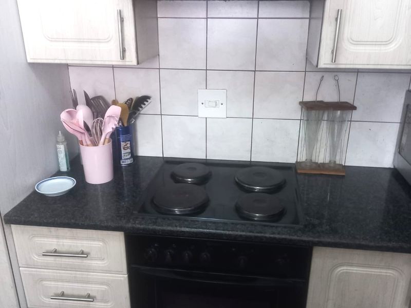 A functional kitchen area featuring built-in cabinetry, a black electric hob with oven, an extractor fan, and a tiled backsplash.