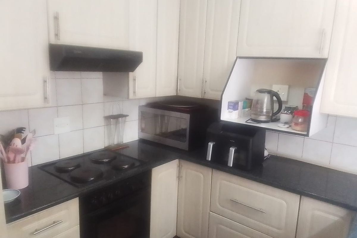 A functional kitchen featuring white cabinetry, dark granite countertops, a built-in oven, electric hob, and an extractor fan with tiled backsplash.