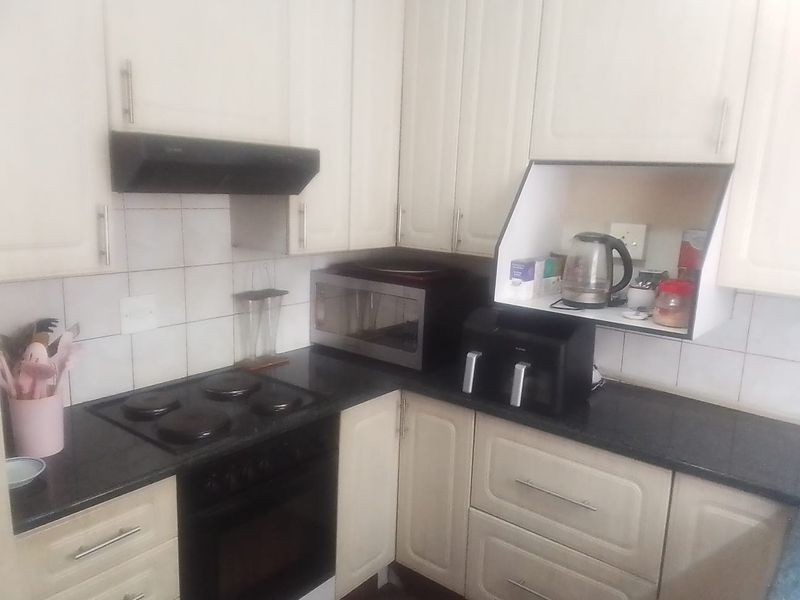 A functional kitchen featuring white cabinetry, dark granite countertops, a built-in oven, electric hob, and an extractor fan with tiled backsplash.