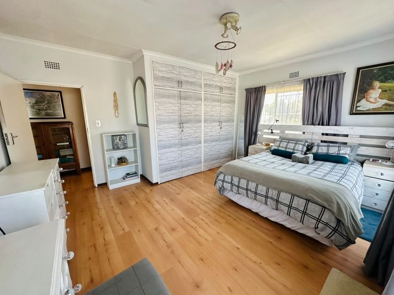 A well-maintained bedroom featuring laminate flooring, built-in cupboards, and a window fitted with a security gate.