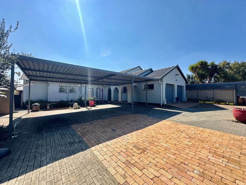 Front exterior view of the property featuring a spacious paved driveway, a large carport, and a double garage with a well-maintained facade.