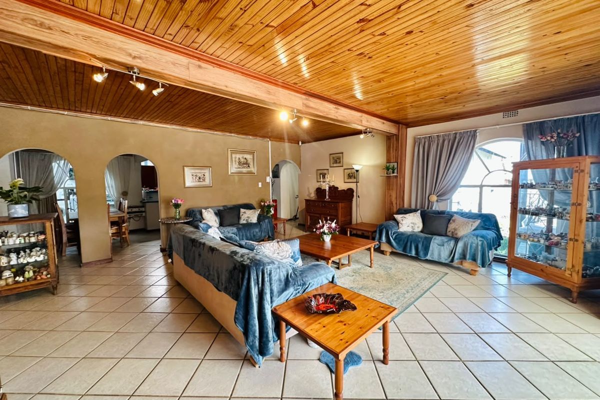 Spacious living area featuring a warm timber tongue and groove ceiling, exposed beams, ceramic tiled flooring, and distinctive arched architectural details.