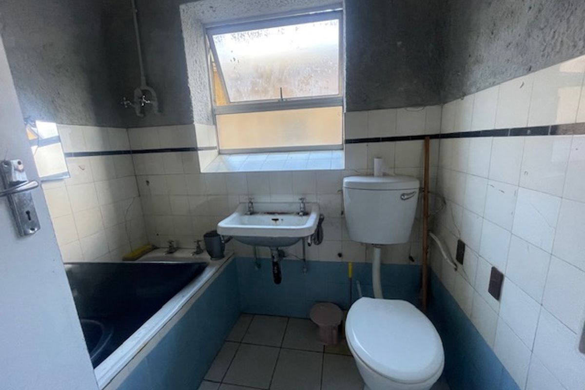 A dated bathroom featuring a bathtub, wall-mounted basin, and toilet, requiring significant renovation and cosmetic updates to improve its condition and functionality.
