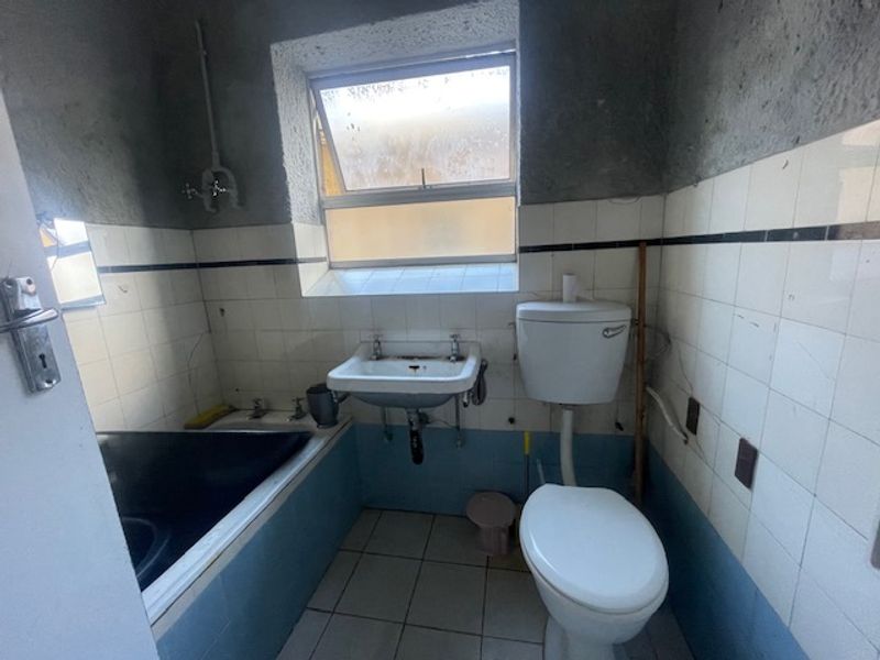 A dated bathroom featuring a bathtub, wall-mounted basin, and toilet, requiring significant renovation and cosmetic updates to improve its condition and functionality.
