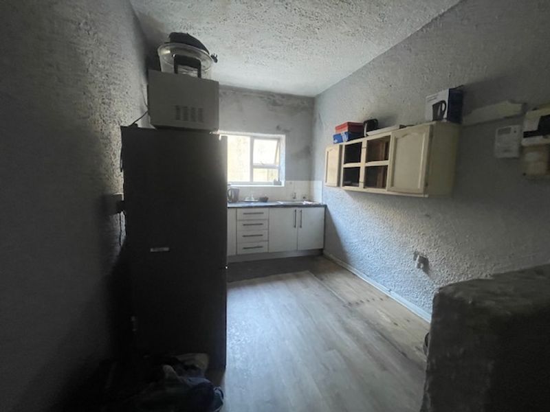 A compact kitchen area featuring basic cabinetry, a sink, and laminate flooring, currently requiring cosmetic updates and repairs to the wall finishes.