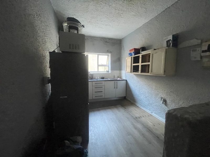 A compact kitchen area featuring basic cabinetry, a sink, and laminate flooring, currently requiring cosmetic updates and repairs to the wall finishes.