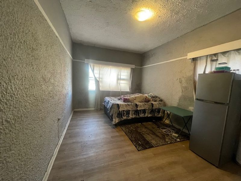 A bedroom featuring textured walls with visible signs of wear and moisture damage, laminate flooring, and a central ceiling light fixture.