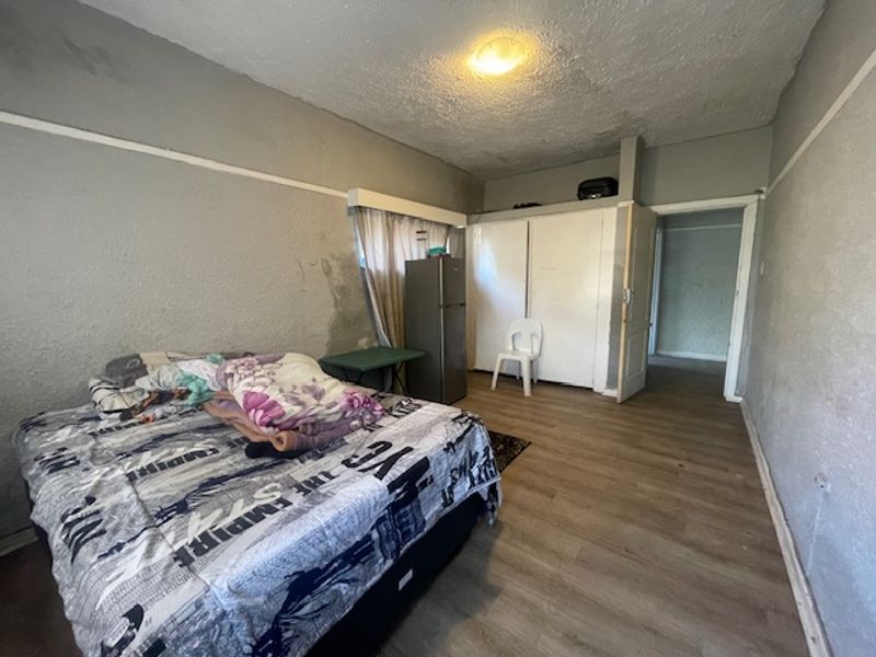 A bedroom featuring laminate flooring and built-in cupboards, currently showing signs of wear and wall surface damage requiring maintenance and cosmetic updates.