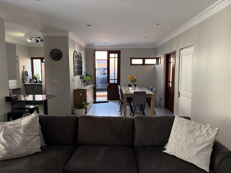 An open-plan living and dining area featuring tiled floors, recessed lighting, and crown molding, with direct access to the exterior through a timber door.